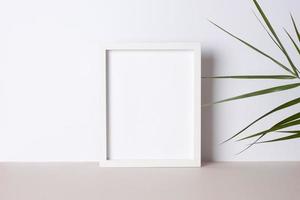 Home decoration with white mock up frame and palm leaf on grey. Artwork showcase. Close up, copy space photo