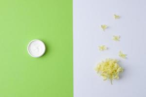 Jar of cosmetic cream with flowers on green and white background. Flat lay, copy space photo