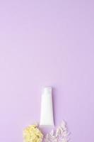 tubo blanco de crema cosmética con flores sobre fondo rosa. endecha plana, espacio de copia foto