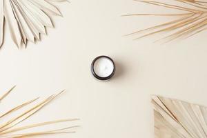 Jar of cosmetic cream with palm leaf on pastel beige background. Flat lay photo