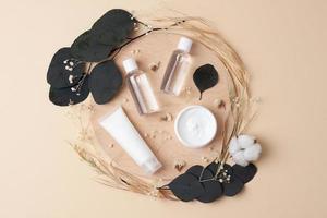 Cosmetic skin care products with flowers and wood on pastel beige background. Flat lay. photo