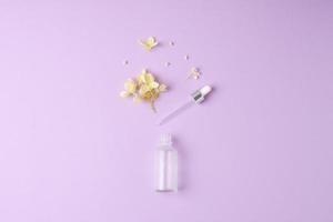 Minimal composition with cosmetic bottle with flowers on rose background. Flat lay, copy space photo