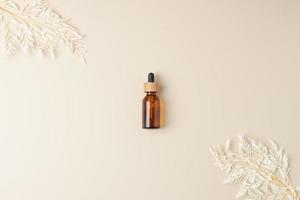 Cosmetic bottle with flowers on pastel beige background. Flat lay, copy space photo