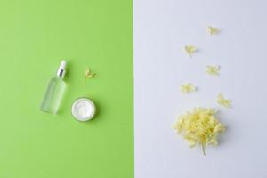 Cosmetic skin care products with flowers on green and white background. Flat lay, copy space photo