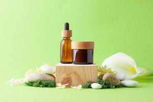 Cosmetic skin care products with wood podium and flowers, moss, stone on green background. Close up, copy space