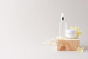 Cosmetic skin care products with wood podium and flowers on grey background. Close up, copy space photo