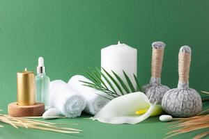 Spa treatment with herbal bag, candles and palm leaf on green background. Close up, copy space photo