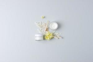 Jars of cosmetic cream with flowers on grey background. Flat lay, copy space photo