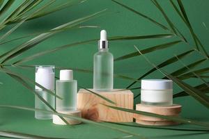 Cosmetic skin care products with wood podium and palm leaf on green background. Close up, copy space photo