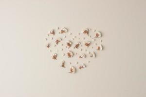 Minimal composition with a heart shape of flowers on pastel beige background. Flat lay, copy space photo