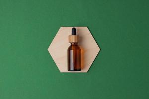Cosmetic bottle with a wooden hexagon on green background. Flat lay, copy space photo