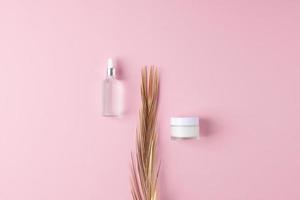 composición mínima con productos cosméticos para el cuidado de la piel y hoja de palma sobre fondo rosa. endecha plana, espacio de copia foto