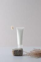 White tube of cosmetic cream on a stone podium with flowers on grey background. Close up. photo