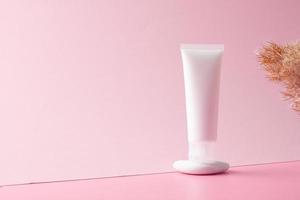 White tube of cosmetic cream on a stone podium with pampas on pink background. Close up, copy space. photo