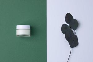 composición mínima con tarro de crema cosmética y eucalipto sobre fondo verde. endecha plana foto