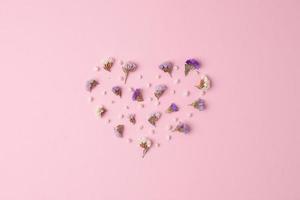 Minimal composition with a heart shape of flowers on pink background. Flat lay, copy space photo
