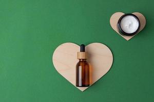 Cosmetic skin care products with a wooden heart on green background. Flat lay, copy space photo