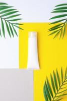 White tube of cosmetic cream with palm on yellow. Flat lay. photo