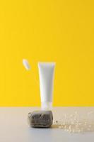 White tube of cosmetic cream on a stone podium with flowers on yellow background. Close up. photo