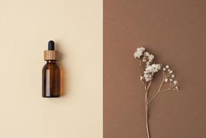 Minimal composition with cosmetic bottle and flowers on pastel beige background. Flat lay, copy space. photo