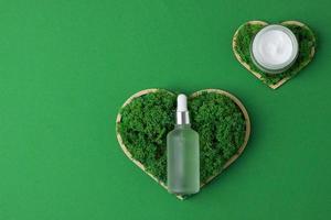 Cosmetic skin care products with a wooden heart and moss on green background. Flat lay, copy space photo