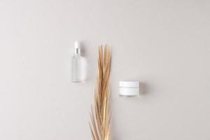 Minimal composition with cosmetic skin care products and palm leaf on grey background. Flat lay photo