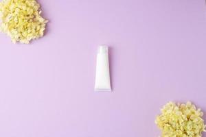 White tube of cosmetic cream with flowers on rose background. Flat lay, copy space photo