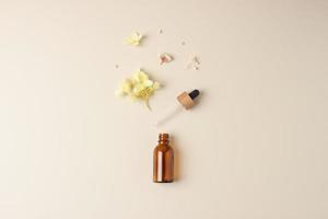 Minimal composition with cosmetic bottle with flowers on pastel beige background. Flat lay, copy space photo