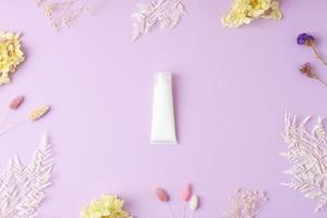 White tube of cosmetic cream with flowers on rose background. Flat lay photo