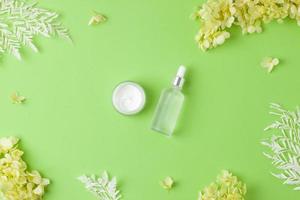 Cosmetic skin care products with flowers on green background. Flat lay photo