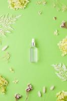 Cosmetic bottle with flowers on green background. Flat lay