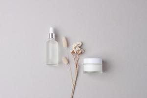 Minimal composition with cosmetic skin care products and flowers on grey background. Flat lay. photo