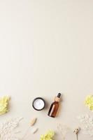 Cosmetic skin care products with flowers on pastel beige background. Flat lay, copy space photo