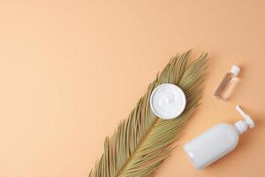 Cosmetic skin care products with palm leaf on pastel beige background. Flat lay, copy space photo