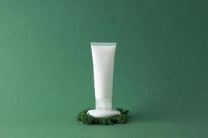 White tube of cosmetic cream on a stone podium with moss on green background. Close up. photo