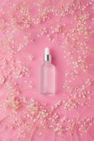 Cosmetic bottle with floral frame on pink background. Flat lay. photo