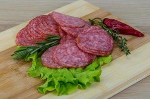 Salami en rodajas sobre tablero de madera y fondo blanco. foto