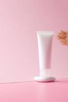 White tube of cosmetic cream on a stone podium with pampas on pink background. Close up. photo