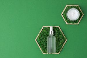 Cosmetic skin care products with a wooden hexagon and moss on green background. Flat lay, copy space photo
