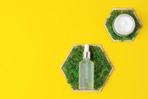 Cosmetic skin care products with a wooden hexagon and moss on yellow background. Flat lay, copy space photo