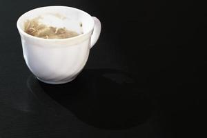 una pequeña taza vacía de café con leche, una pequeña taza sucia de cerámica usada de capuchino, un tazón pequeño con acabado blanco de expresso aislado en la mesa negra, nadie vajilla de café, primer plano, arte. foto