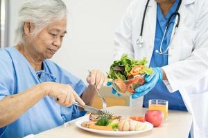 Asian senior or elderly old lady woman patient eating breakfast and vegetable healthy food with hope and happy while sitting and hungry on bed in hospital. photo