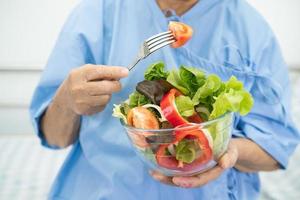 Asian senior or elderly old lady woman patient eating breakfast vegetable healthy food with hope and happy while sitting and hungry on bed in hospital. photo