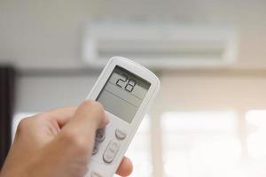 Hand with remote control directed on air conditioner inside the room photo