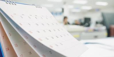 Close up white paper desk calendar on table with blurred office interior background photo