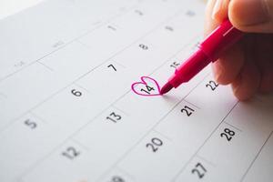 Female Hand with pen mark heart shape on calendar date at 14th valentine day photo