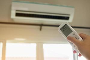 Hand with remote control directed on air conditioner inside the room photo