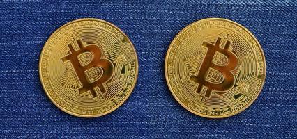 Two golden Bitcoins is lies on a blue jeans fabric. New virtual money. New crypto currency in the form of the coins photo