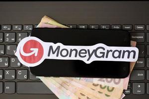 TERNOPIL, UKRAINE - SEPTEMBER 6, 2022 MoneyGram paper logotype lies on black laptop with ukrainian hryvnias. Moneygram is American cross border P2P payments and money transfer company photo