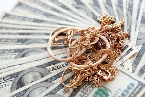 muchos costosos anillos de joyería de oro, aretes y collares en una gran cantidad de billetes de dólares estadounidenses de cerca. casa de empeño o joyería foto